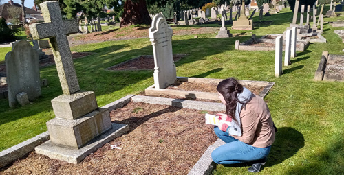 Young woman kneels by a war grave