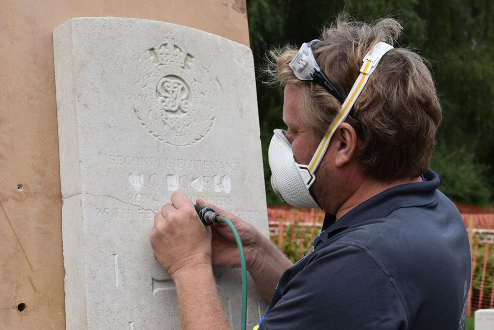 Man inscribing letters on a CWGC headstone using an electric tool.