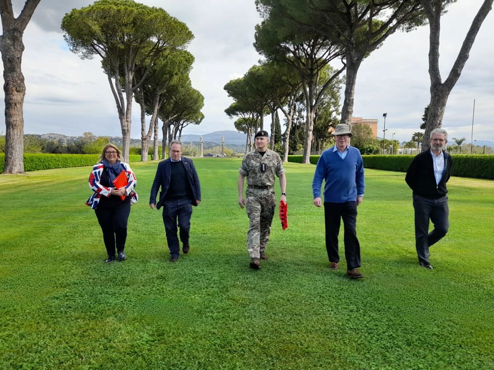 Five people walking across the lawn at Minturno War Cemetery, Italy.